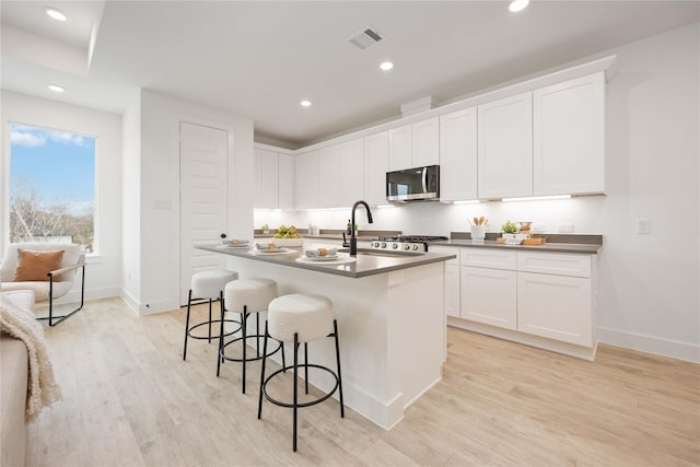 kitchen with a sink, a kitchen breakfast bar, dark countertops, stainless steel microwave, and visible vents