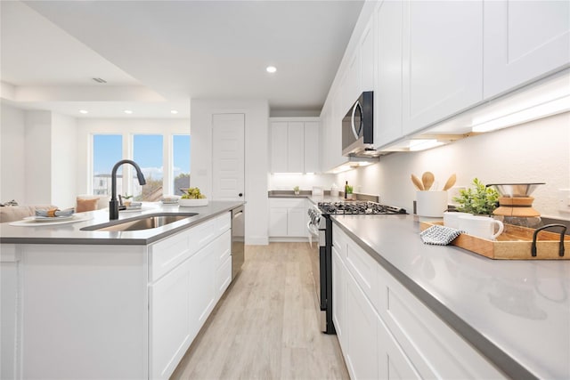 kitchen featuring white cabinets, recessed lighting, appliances with stainless steel finishes, a sink, and light wood-style floors