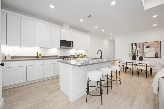 kitchen with stainless steel microwave, a sink, light wood-style floors, and recessed lighting