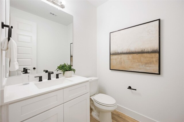 bathroom featuring visible vents, baseboards, toilet, wood finished floors, and vanity