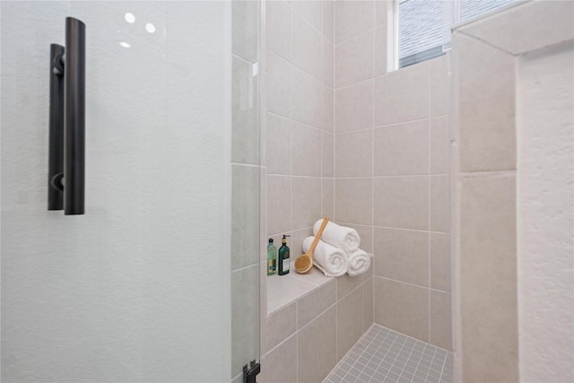 bathroom with a textured wall and tiled shower