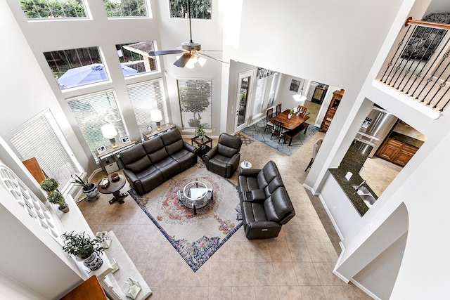 living area featuring tile patterned floors, a towering ceiling, baseboards, and ceiling fan