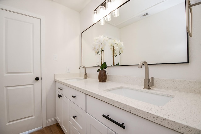 full bath featuring wood finished floors, visible vents, a sink, and double vanity