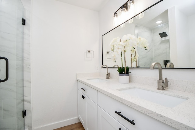full bathroom with baseboards, a sink, double vanity, and a stall shower