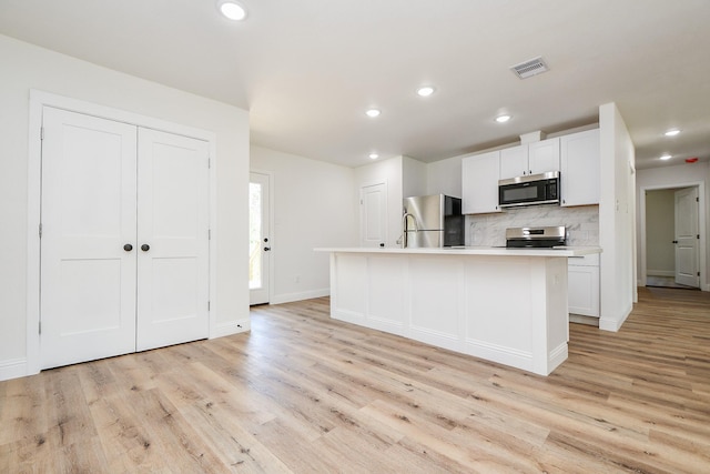 kitchen with stainless steel appliances, tasteful backsplash, visible vents, light wood-style floors, and an island with sink