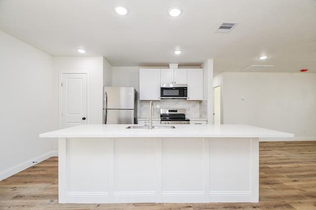 kitchen with a sink, an island with sink, stainless steel appliances, light countertops, and baseboards