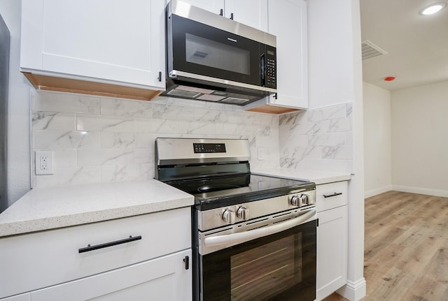 kitchen with tasteful backsplash, appliances with stainless steel finishes, white cabinetry, light stone countertops, and visible vents