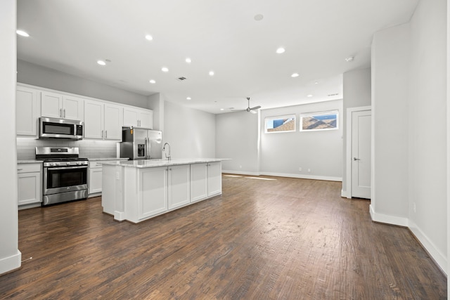 kitchen with dark wood finished floors, decorative backsplash, appliances with stainless steel finishes, baseboards, and a center island with sink
