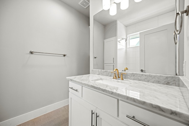 full bath featuring a tile shower, visible vents, vanity, and baseboards