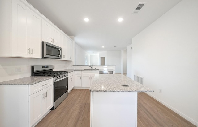 10710 Sora Dr, Willis, TX 77378 - kitchen featuring stainless steel appliances, a sink, a peninsula, light wood-style flooring, and a kitchen island