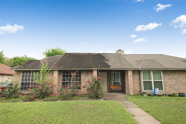 single story home with brick siding, a chimney, roof with shingles, and a front yard