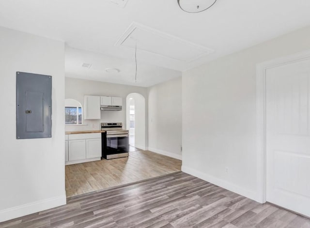 kitchen featuring under cabinet range hood, arched walkways, stainless steel range with electric cooktop, light wood-style flooring, and electric panel