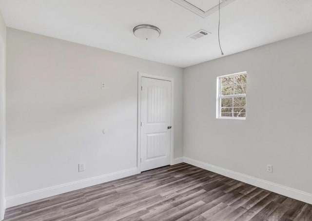 spare room featuring attic access, baseboards, visible vents, and wood finished floors