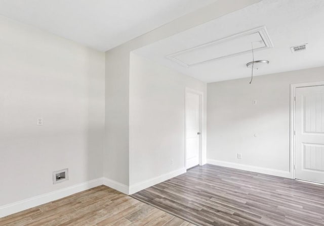 empty room featuring baseboards, visible vents, wood finished floors, and attic access