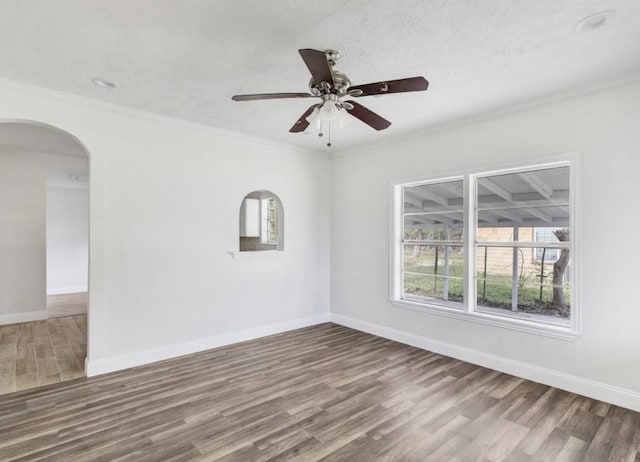 unfurnished room with baseboards, arched walkways, wood finished floors, and ornamental molding