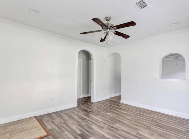 empty room with a ceiling fan, wood finished floors, baseboards, visible vents, and ornamental molding
