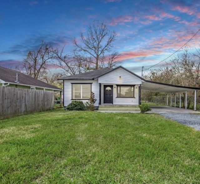 bungalow featuring a front lawn, driveway, a carport, and fence