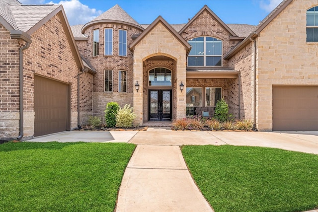 view of exterior entry with brick siding, driveway, a yard, and french doors