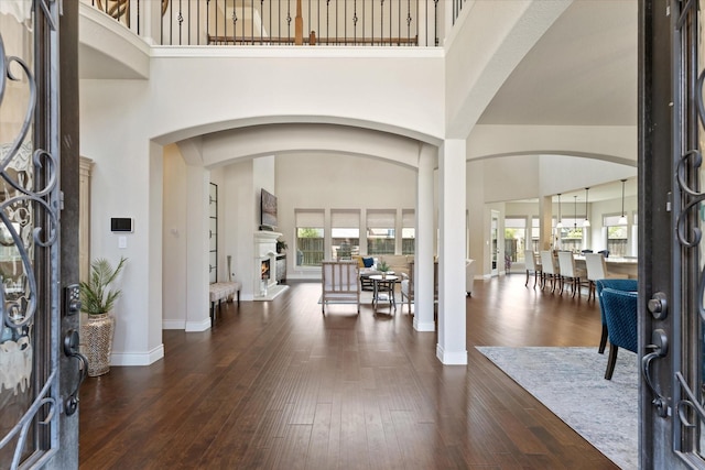 entrance foyer featuring baseboards, a high ceiling, a lit fireplace, and wood-type flooring