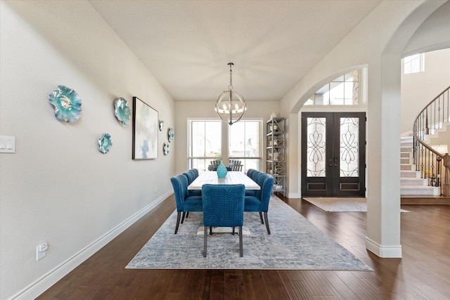 dining space featuring plenty of natural light, arched walkways, a notable chandelier, and stairway