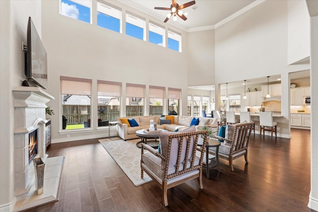 living area featuring crown molding, a high end fireplace, ceiling fan, a high ceiling, and dark wood-style floors