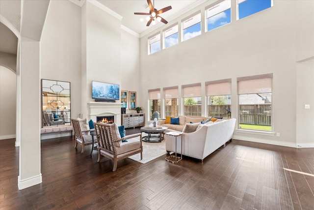 living area with crown molding, ceiling fan, arched walkways, a lit fireplace, and dark wood finished floors