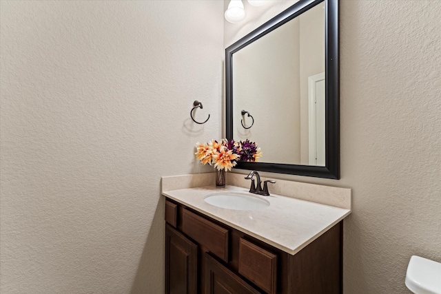 bathroom with a textured wall, vanity, and toilet