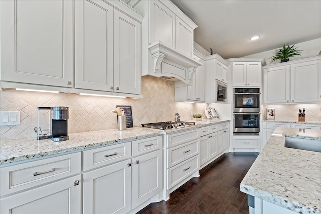 kitchen with tasteful backsplash, white cabinets, stainless steel appliances, custom range hood, and dark wood finished floors