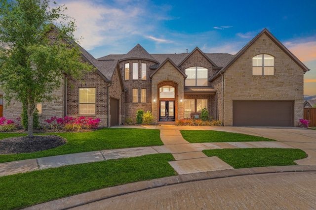 french country inspired facade featuring french doors, concrete driveway, a garage, brick siding, and a lawn