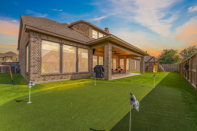 back of property at dusk featuring brick siding, a ceiling fan, a patio, and a playground