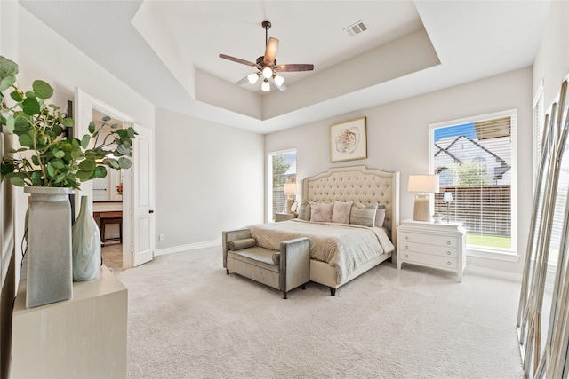 bedroom with light carpet, a tray ceiling, baseboards, visible vents, and a ceiling fan