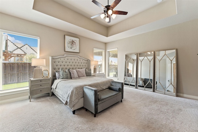 carpeted bedroom with a ceiling fan, baseboards, a raised ceiling, and multiple windows