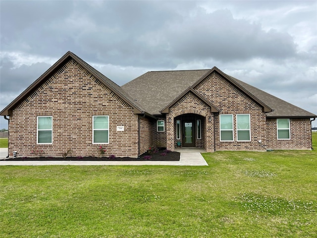 view of front of home with brick siding, roof with shingles, and a front lawn