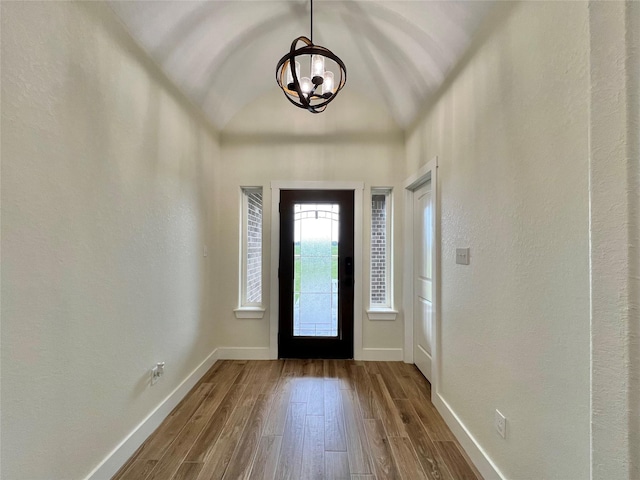 foyer entrance featuring a textured wall, a notable chandelier, baseboards, and wood finished floors