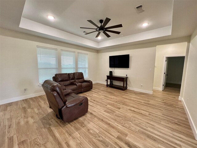 living area with a tray ceiling, light wood-style flooring, and a ceiling fan