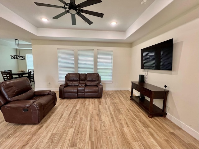 living area featuring baseboards, ceiling fan, light wood-type flooring, and a raised ceiling