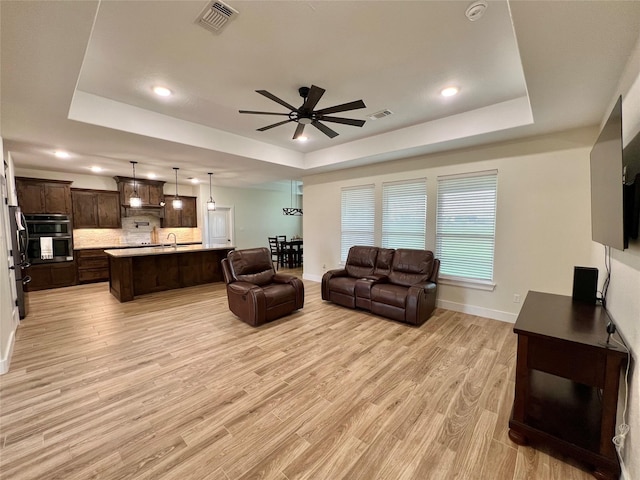living room featuring light wood-style flooring, visible vents, a ceiling fan, and a raised ceiling