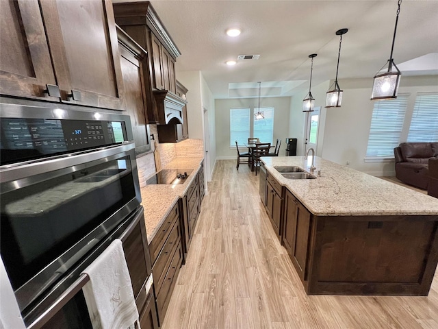 kitchen featuring double oven, a sink, dark brown cabinetry, and visible vents