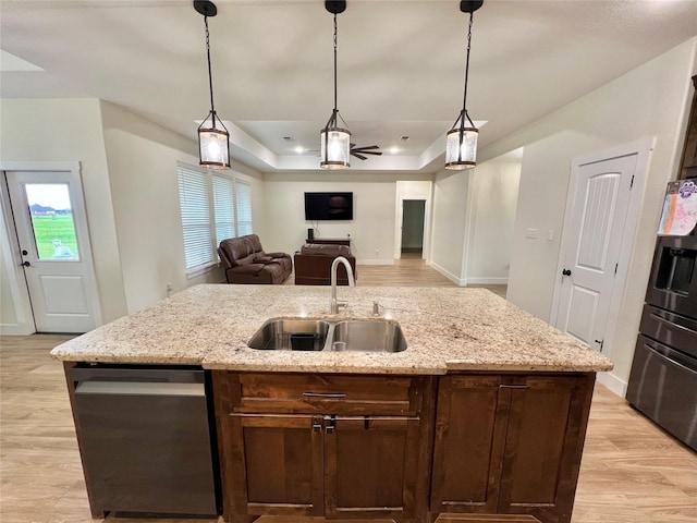kitchen featuring a sink, a raised ceiling, stainless steel dishwasher, open floor plan, and light wood-style flooring