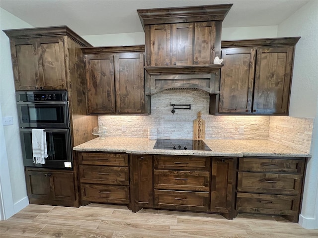 kitchen with black appliances, decorative backsplash, light stone counters, and dark brown cabinets
