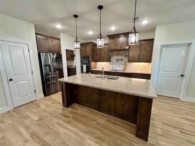 kitchen featuring stainless steel refrigerator with ice dispenser, a sink, light wood finished floors, dark brown cabinets, and dobule oven black
