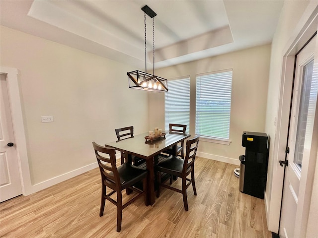 dining room featuring a raised ceiling, a notable chandelier, baseboards, and light wood-style floors