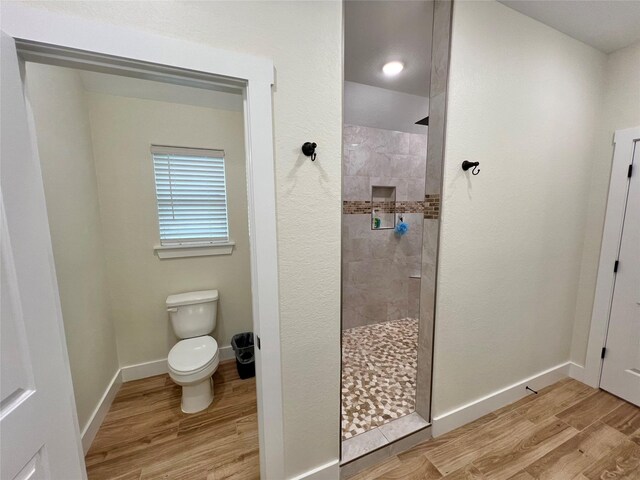bathroom featuring baseboards, wood finished floors, toilet, and walk in shower