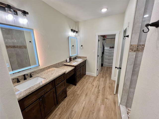 full bathroom with a sink, tiled shower, and wood finished floors