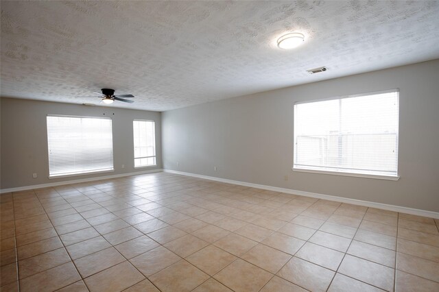 spare room featuring light tile patterned flooring, ceiling fan, a textured ceiling, baseboards, and visible vents
