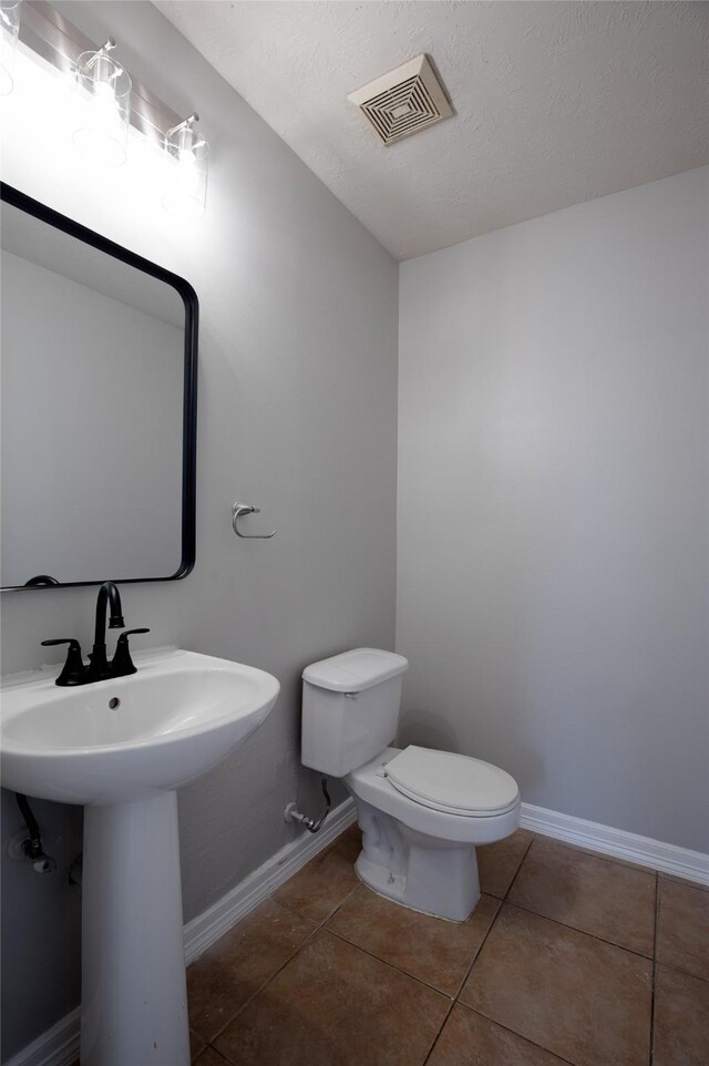 half bath with toilet, tile patterned floors, visible vents, and baseboards