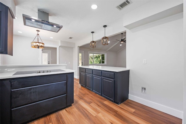kitchen featuring light countertops, visible vents, wall chimney range hood, light wood-style floors, and a peninsula