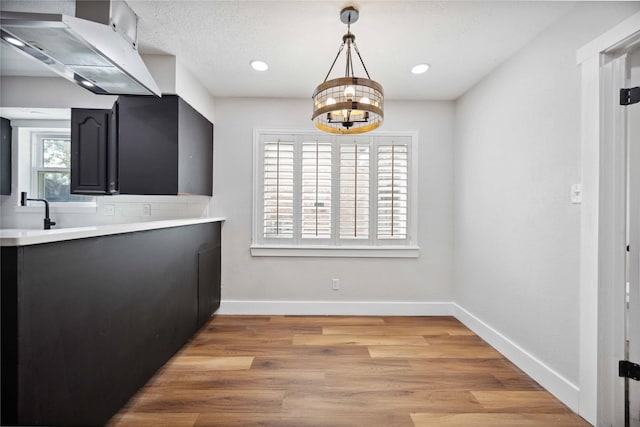 kitchen featuring a chandelier, light wood finished floors, light countertops, baseboards, and under cabinet range hood