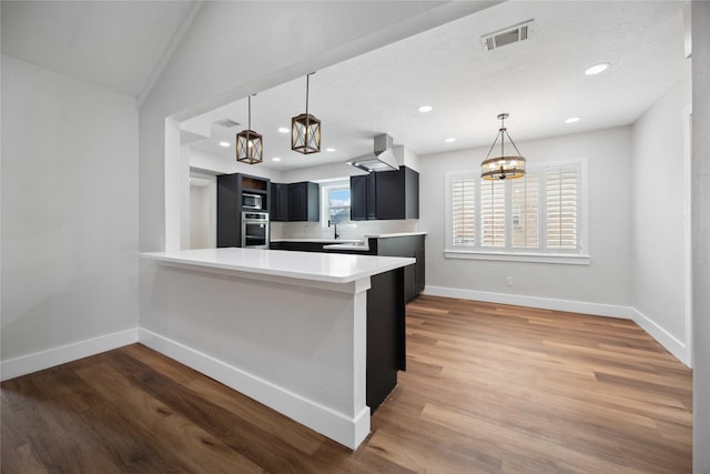 kitchen featuring light countertops, wall chimney range hood, baseboards, a peninsula, and stainless steel oven