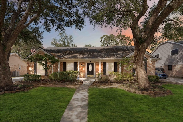 ranch-style house featuring brick siding, a yard, and central air condition unit